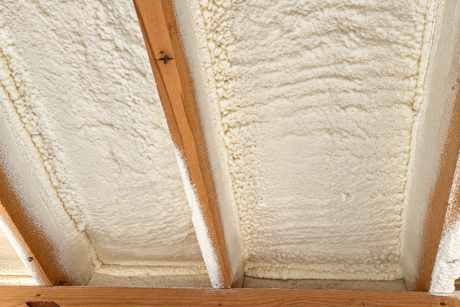 Close view of cream spray foam filling the spaces between exposed wooden ceiling joists.