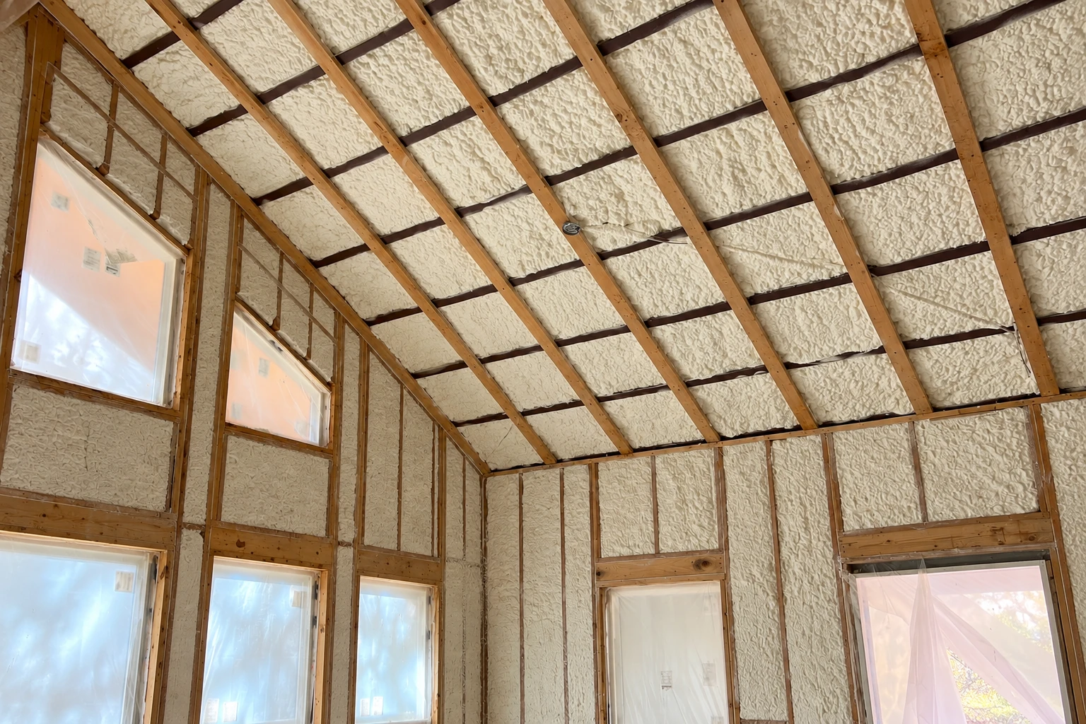 Open room with cream spray foam covering the sloped roof and walls between exposed wooden framing.