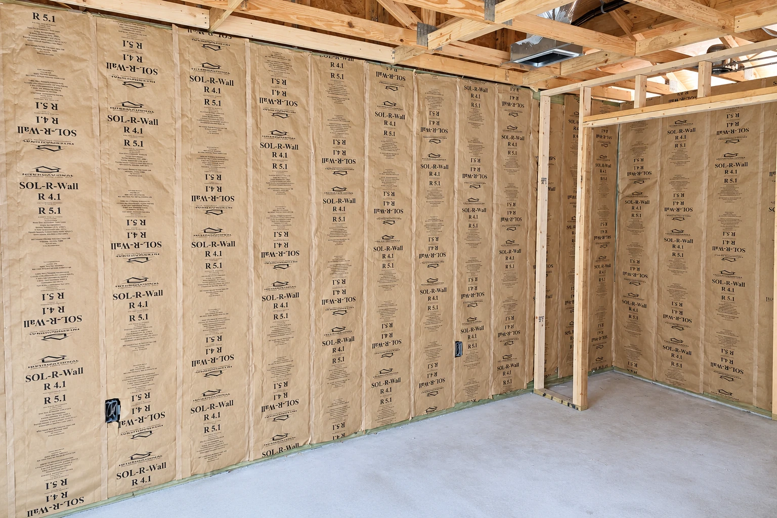 Unfinished commercial space with tan batt insulation fitted between wall studs beneath exposed wooden roof framing.