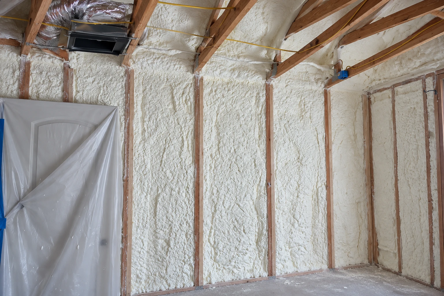 Foam insulation fills the wall cavities and ceiling of an unfinished room, with a plastic sheet covering a doorway.