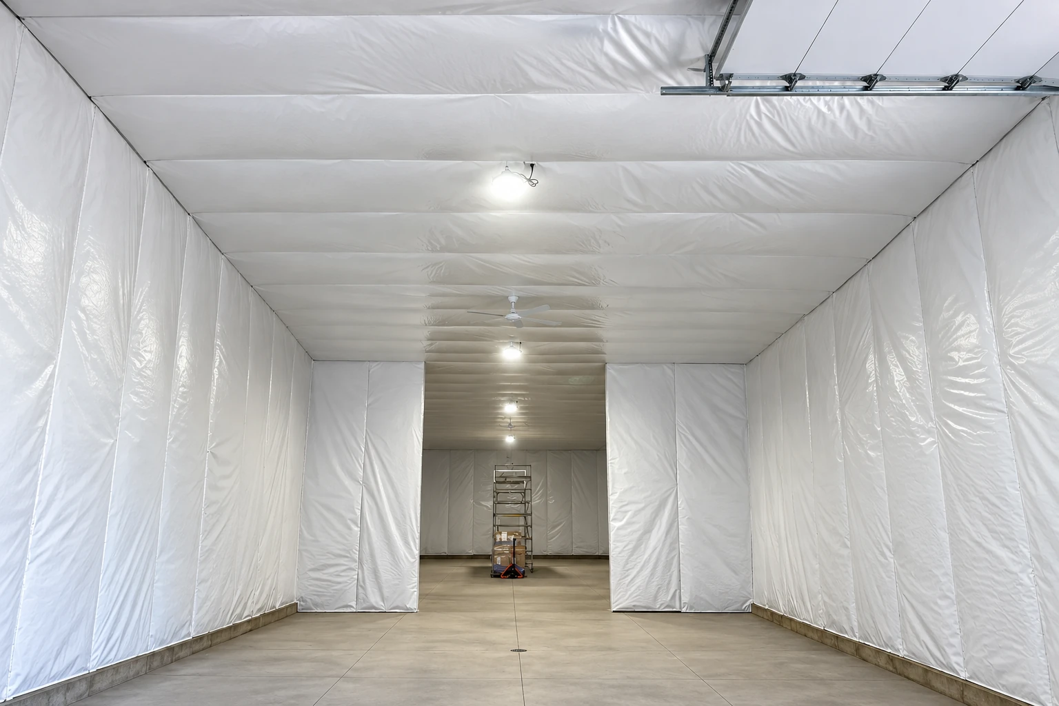 White vapor barrier sheeting covers the walls and ceiling of a long indoor space with a concrete floor.