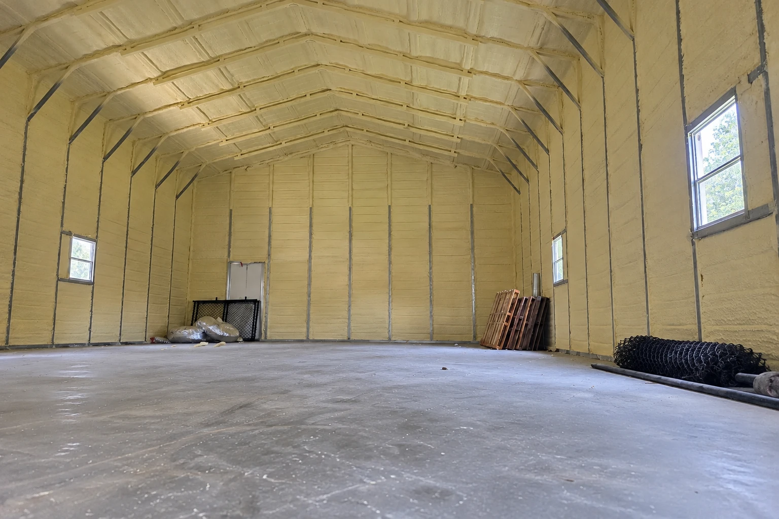 Yellow spray foam covers the walls and arched ceiling of a large, empty building.